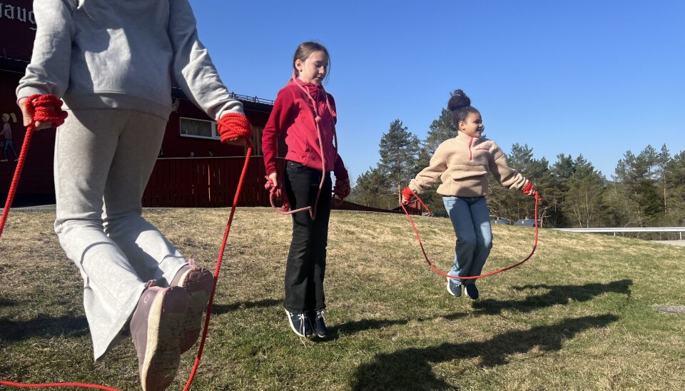 Sola strålte for hopperne hele skoleuka. tre jenter hopper hoppetau på gress med blå himmel bak
