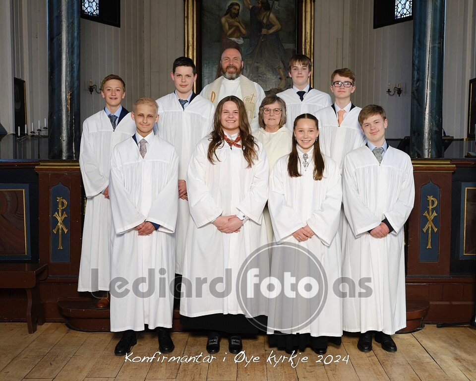 Konfirmantene i Øye kyrkje Åtte konfirmantar i kvite kapper, ei dame i kvit kappe, og ein prest.