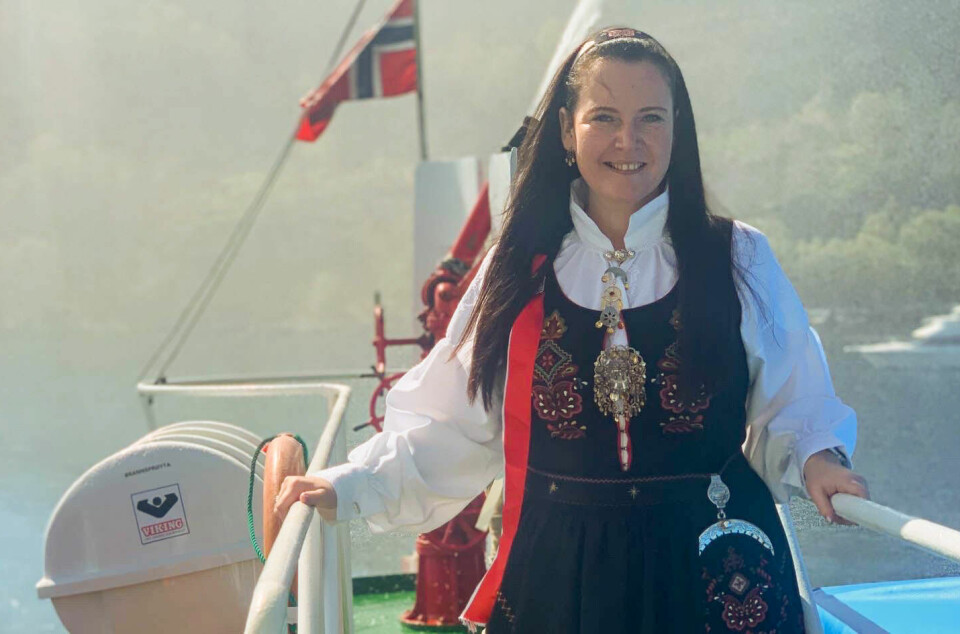 Ei dame i bunad med et norsk flagg i bakgrunnen.