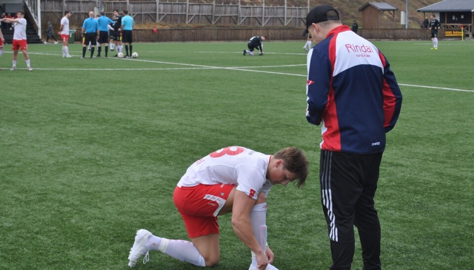 Trenar Lars Ole Heggem med siste formaningar til Mikkel Bakken før kamp. spiller i drakt knyter sko ved siden av trener på fotballbane