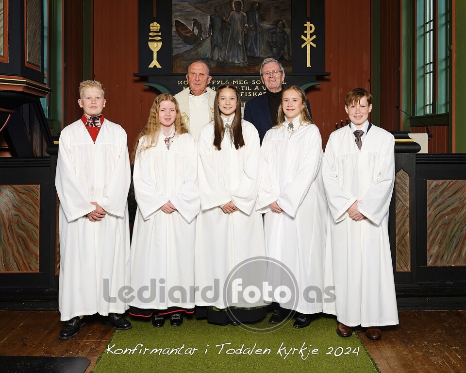 Konfirmantane i Todalen kyrkje Fem konfirmanter i hvite kapper oppstilt i koret i kirka, sammen med en prest og en mann kledd i dress.