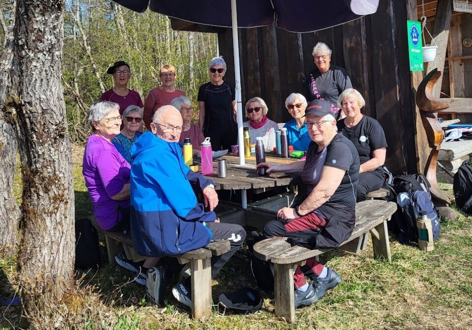 Rast ved elvepromenaden En gruppe mennesker raster ved et bord med parasoll over.