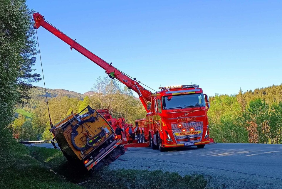 To tungbilbergere som drar opp en lastebil som har kjørt utfor veien.