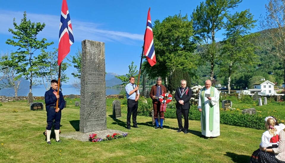 Flaggborg og sang på graven til Halvor Røen. to menn holder to norske flagg ved stor grav, prest og ordfører ved siden av