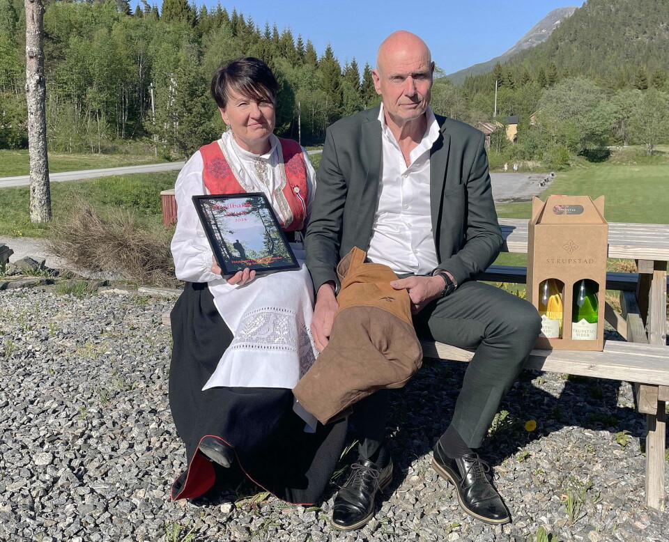 Vinnarane med diplomet og gåva etter tildelinga. Men anerkjennelsen betyr mest. Ei bunadskledd dame og en mann i dress som sitter på en benk.