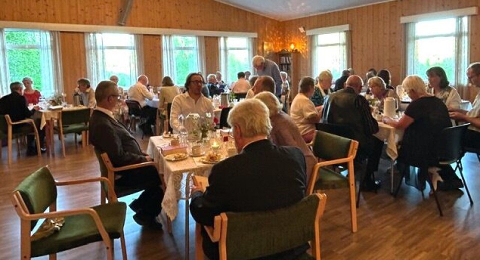 Ein del av festlyden. Mange mennesker som sitter ved små bor di et forsamlingshus.