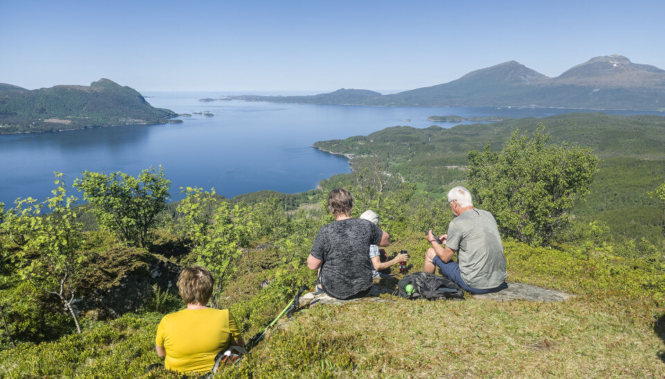 Vidt utsyn frå Aakvik-knoken 374 moh. (bilde tatt ved en tidligere anledning) Fire turkledde personer som sitter på et berg og ser utover fjorden.