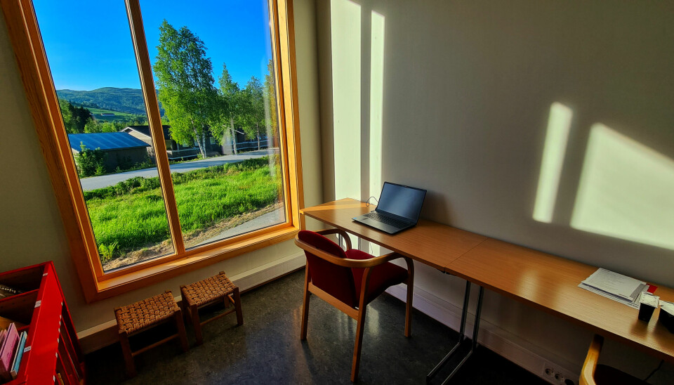 En datamaskin står på et bord stilt inntil veggen ved siden av et vindu