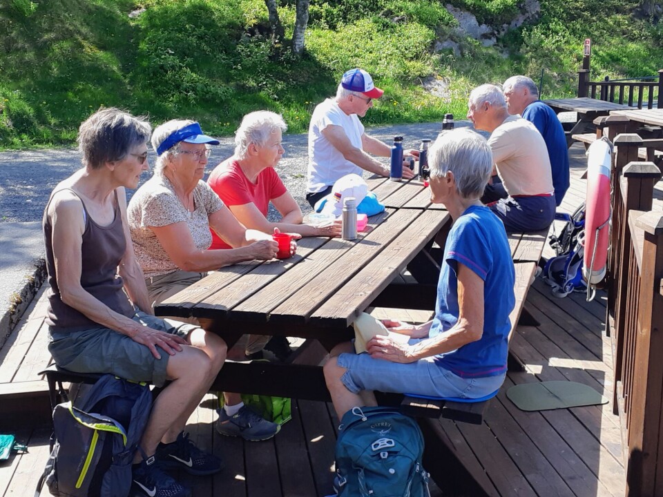 Ei lita gruppe med pensjonister som sitter ved bord ved en rasteplass ved sjøen.