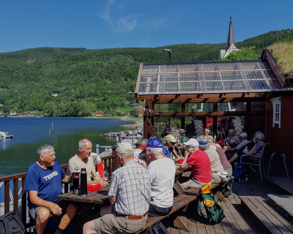 Ei lita gruppe pensjonister som sitter ved bord på en rasteplass ved sjøen.