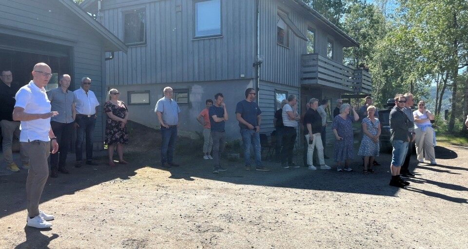 Kommunestyret på befaring på den eventuelle tomta for A+. Mange mennesker som står ved et hus, i solskinn.