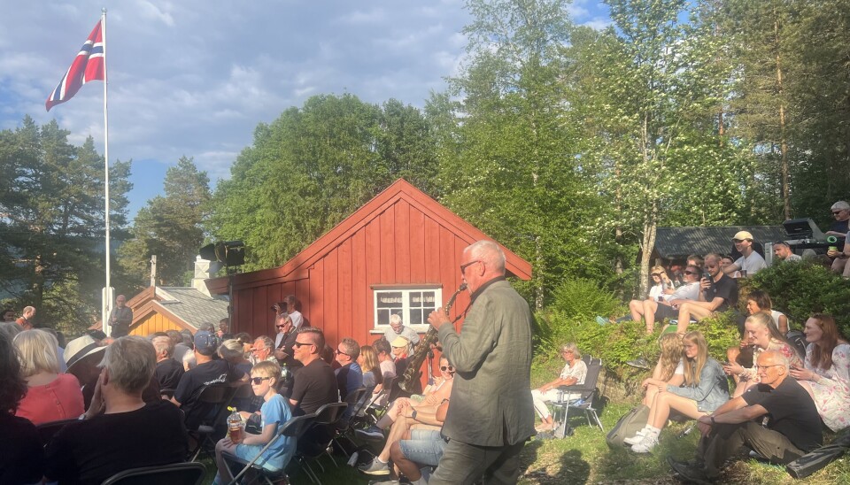 John Pål Indergård spelte midt i folkemengda på Kleiva. mann med saksofon midt i publikum ute, flagg og hus i bakgrunnen