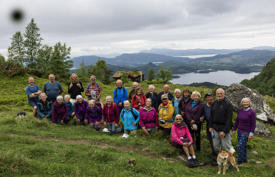 Alle 25 er glade for at skodda letta til nedturen. Ei gruppe turgåere og en hund oppstilt til fotografering med fin utsikt i bakgrunnen.