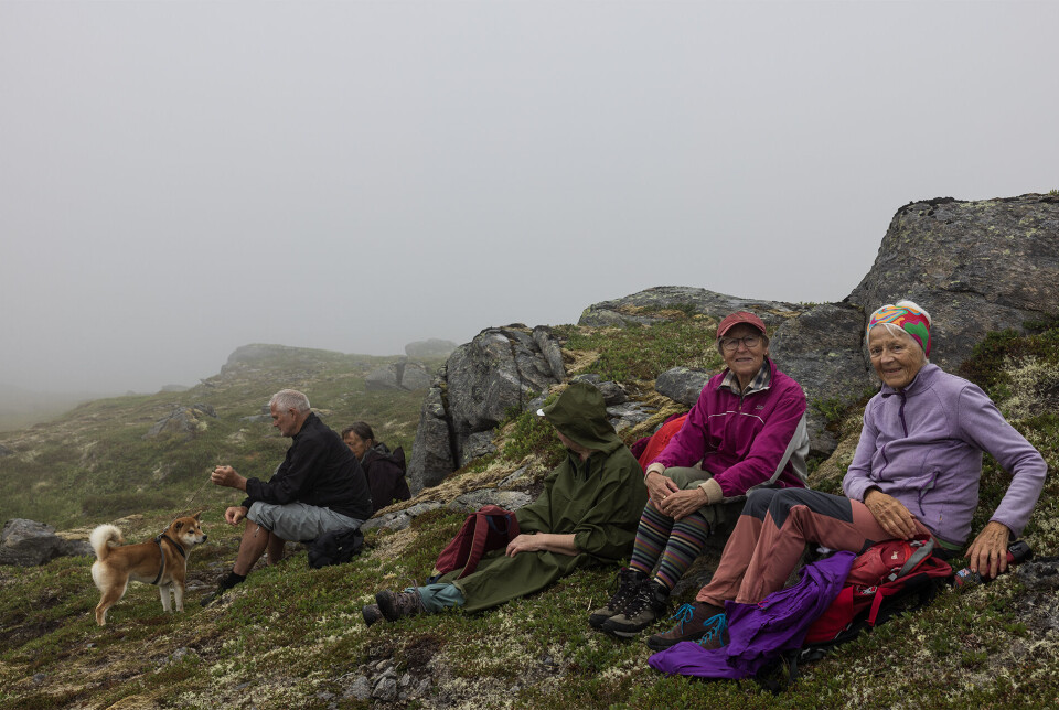 Matpause i ly like under Fløystadfjellets topp. Noen turgåere som har tatt en rast på fjellet, med tåke rundt.