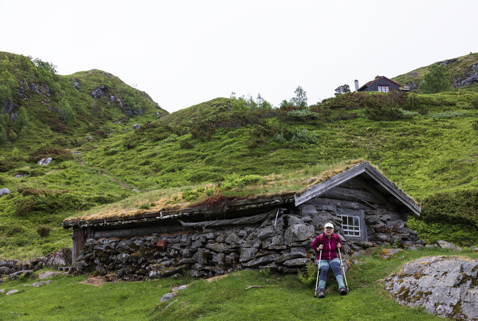 Ein kvil ved det vakre gamle fjøset på Nysetra før siste etappe ned. Ei dame med gåstaver som har satt seg ned for å hvile på en gammel seterstøl.