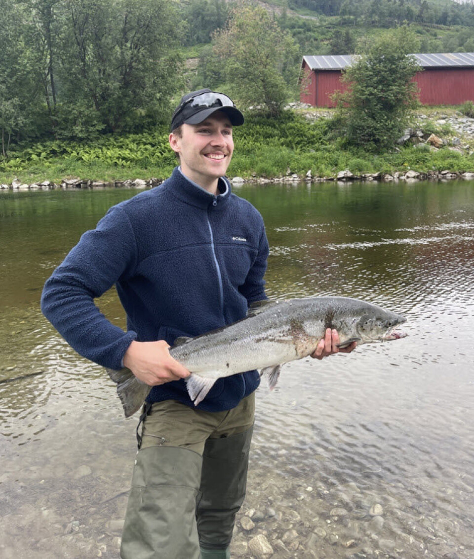 Kasper Ringvold med den første laksen i Surna i år. mann holder laks foran elv.