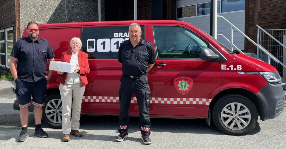 Linda White kom med bløtkake til feierne. Ei eldre dame og to menn i brannvesen-skjorter, som står foran en redningsbil.