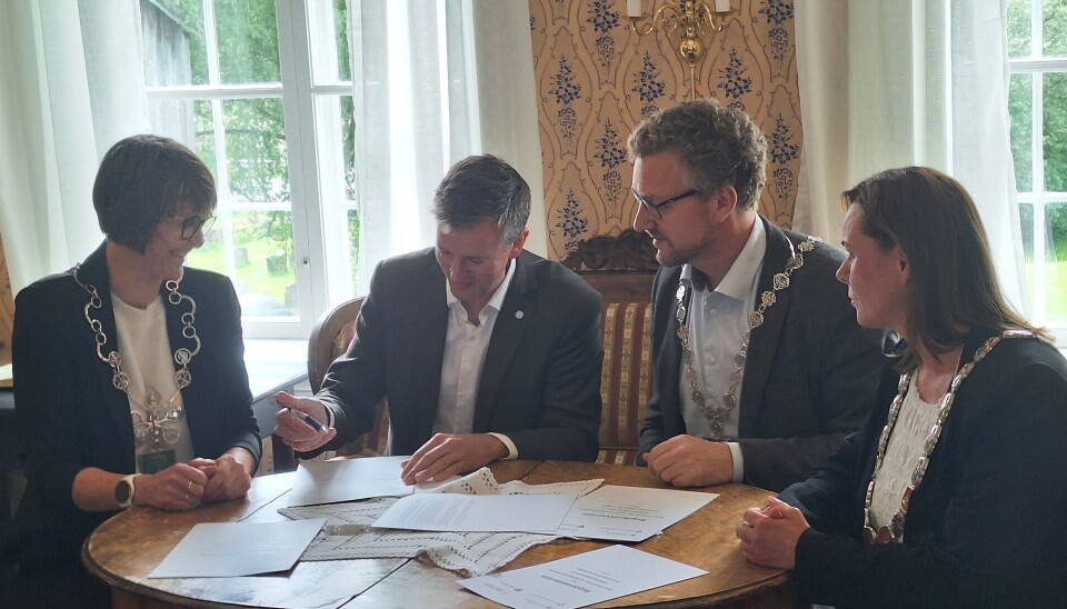 Kommunal- og distriktsminister Erling Sande signerer avtalen. Til høyre ordfører Mildrid Kattem Aune. Til venstre for statsråden fylkesordfører i Trøndelag Tomas Iver Hallem og varaordfører i Holtålen Liv Grete Heksem. Fire personer rundt et bord med papirer.