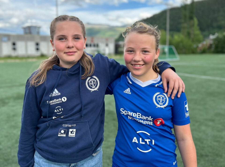 Maja Kristine Moe og Ellen Helgetun Schei gleder seg stort til Driva Cup. To smilende jenter i idrettslagsdrakt på en fotballbane.