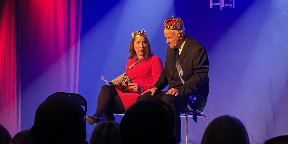 Kongen og Dronningen spilt av Lars Settemsdal og Ingunn Settemsdal. En kvinne i rød kjole og en mann med dress sitter på scena. Begge har på krone på hodet