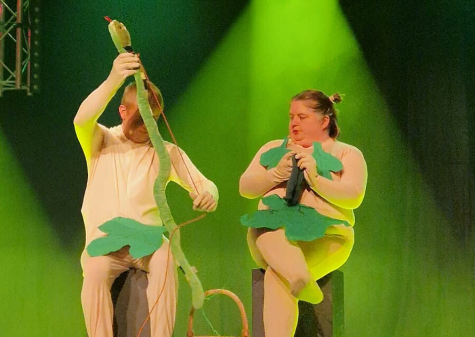 Eva og Andre diskuterer hvem som skal levere ved neste pappahelg To person sitter på en scene, de har på hudfarget drag og fikenblad over utsatte steder. Ene personen holder en slange, den andre strikker