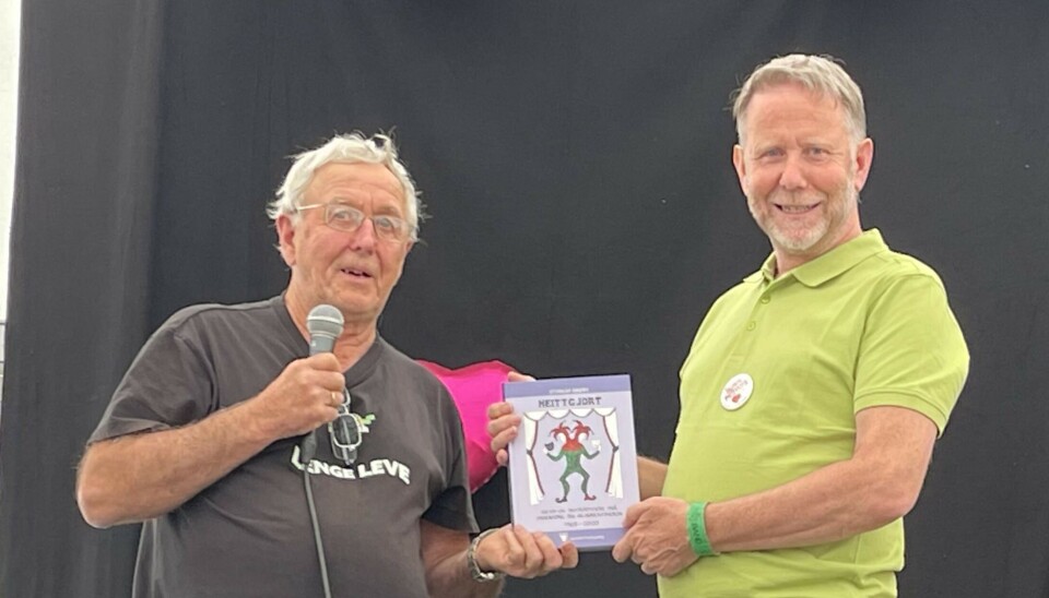 Overrekkelse av boke Heittgjort fra Øyvind Holte til Svein Waade på vegen av Humorfestivalen En menn i svart t-skjorte leverer ei bok til en mann i grønn skjorte