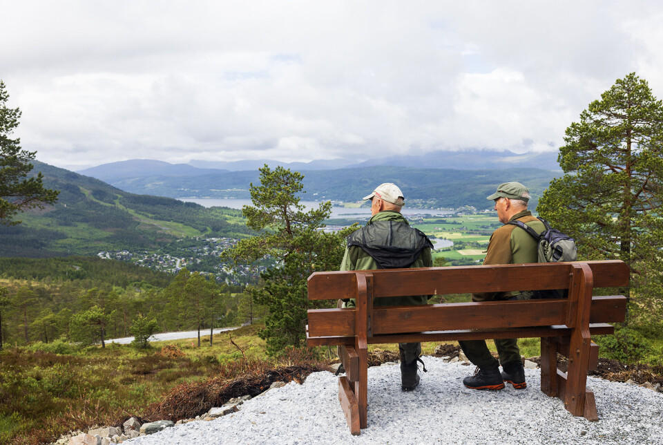 Nyter utsikten frå Malibu. To turkledde menn som sitter på en benk i marka og nyter utsikten ned mot bygda.