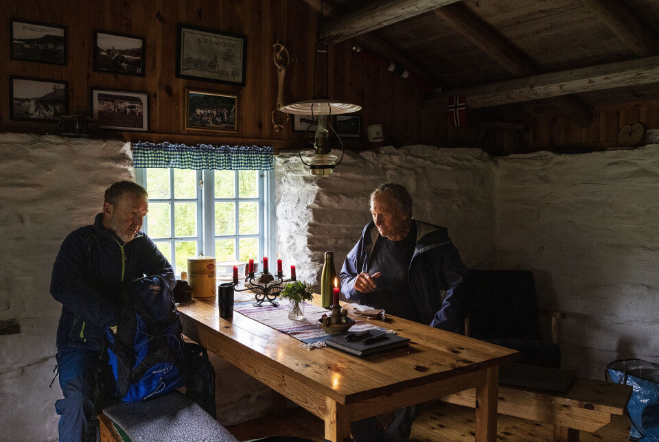 Nostalgi og hygge inne i seterskjelet. To menn ved et bord inne i en gammel steinbygning.