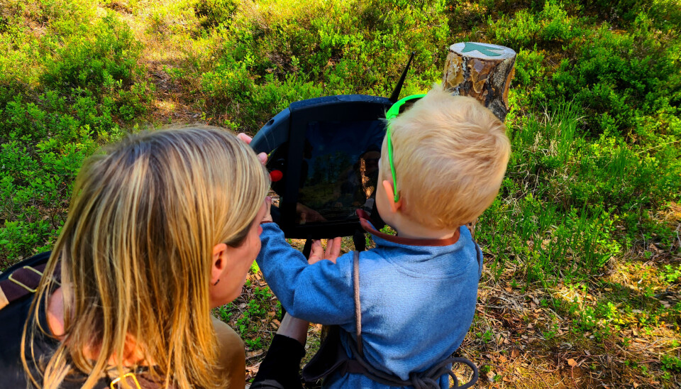 La trollforskningen begynne! Et barn ser på en 'pad' og snakker med to troll. En voksen sitter ved siden av og hjelper med å holde paden oppe.
