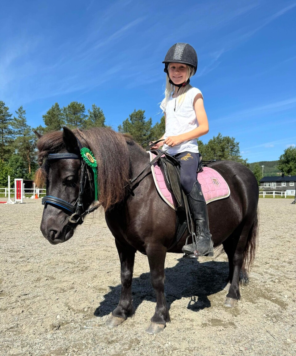 Guro Engset Gravvold er fornøyd med ponnien sin Lahamar Sky etter en fin runde. Smilende jente på en svart ponni som har fått grønn sløyfe