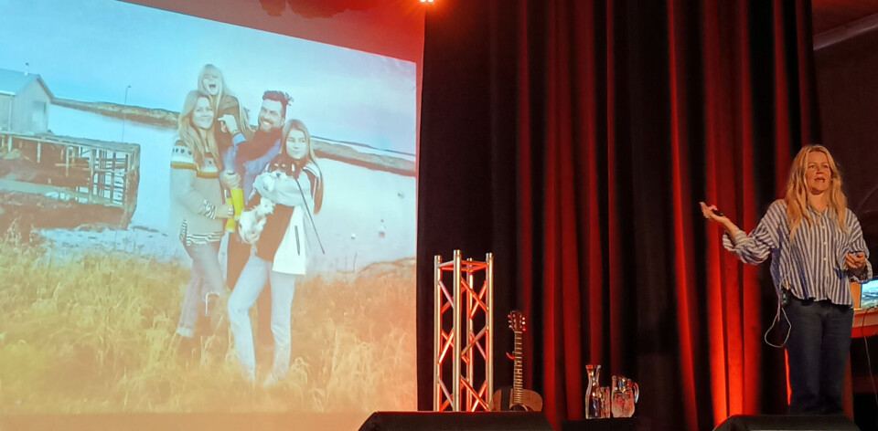 Ingrid Erøy Fagervik fortalte om da familien flyttet til Seløy Ei dame foran en stor skjerm på scenen. På skjermen vies bilde av henne selv, henne mann og to barn, med havet i bakgrunnen.