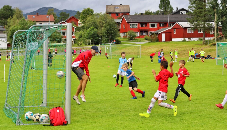 Gruppe 3 (G 2015-2016) avslutter mandagens 2. økt med fotballkamp mellom instruktører mot deltagere. Her er det deltager-laget som skårer på instruktør Geir Magne Glåmen. Vi ser ballen går i mål, med 4-5 gutter i angrep. Voksen mann i mål prøver å redde. Flere baner i bakgrunnen med fotballaktivitet kan skimtes.