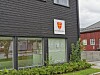 Mørk trebygning med skilt for Rindal kirkekontor og grønne busker foran.