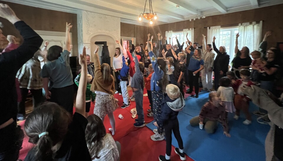 Så opp blir ned, og ned blir opp! mange barn og voksne i rom med handa opp