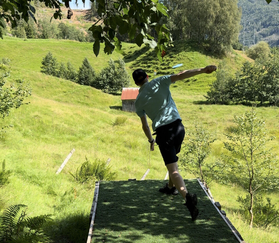 Nordmørstour på Sagdammen diskgolfpark En person med ryggen mot fotografen, idet han kaster en frisbee på en diskgolfbane.