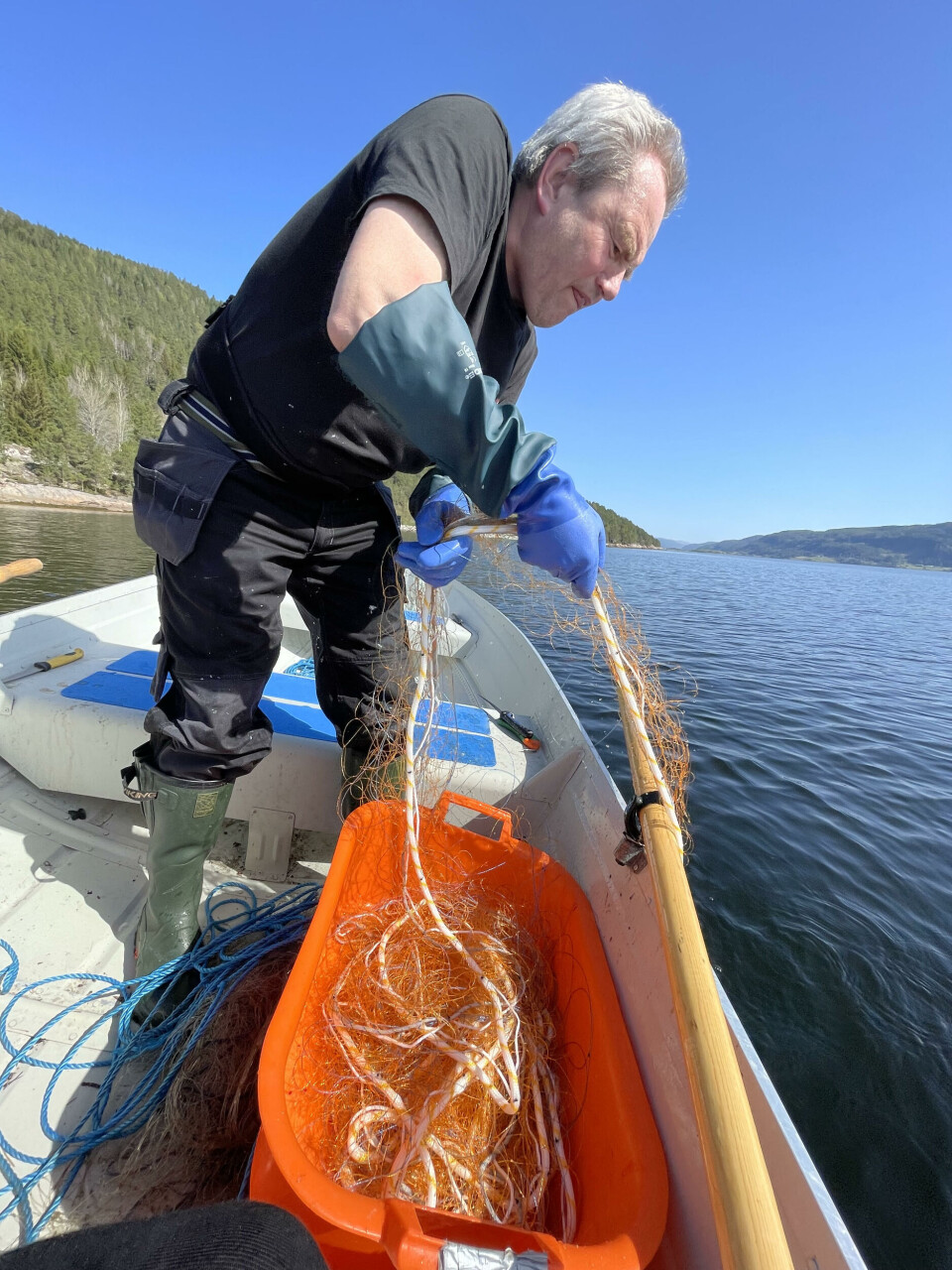 en mann drar opp et fiskegarn opp i en båt