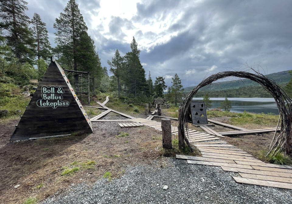 Boll og Bøllus lekeplass for små og store troll. En portal med en sti gjennom. En trekantet treboks med klatremuligheter. Skog, fjell og vann i bakgrunn