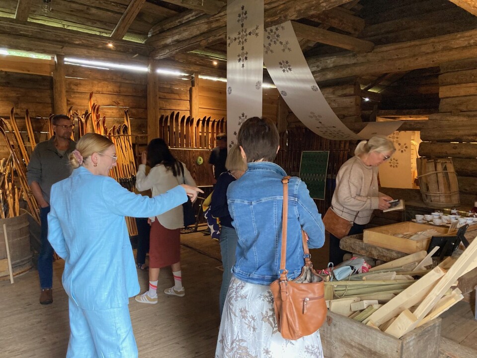 Flere skuelystne hadde møtt opp for å se arbeidsutstillingen på Skimakerlåven denne fredagen. Folk som ser jeg rundt i skimakerlåven, omgitt av både ski og kunsttrykk. Kunstneren står midt i bildet og peker på noe.