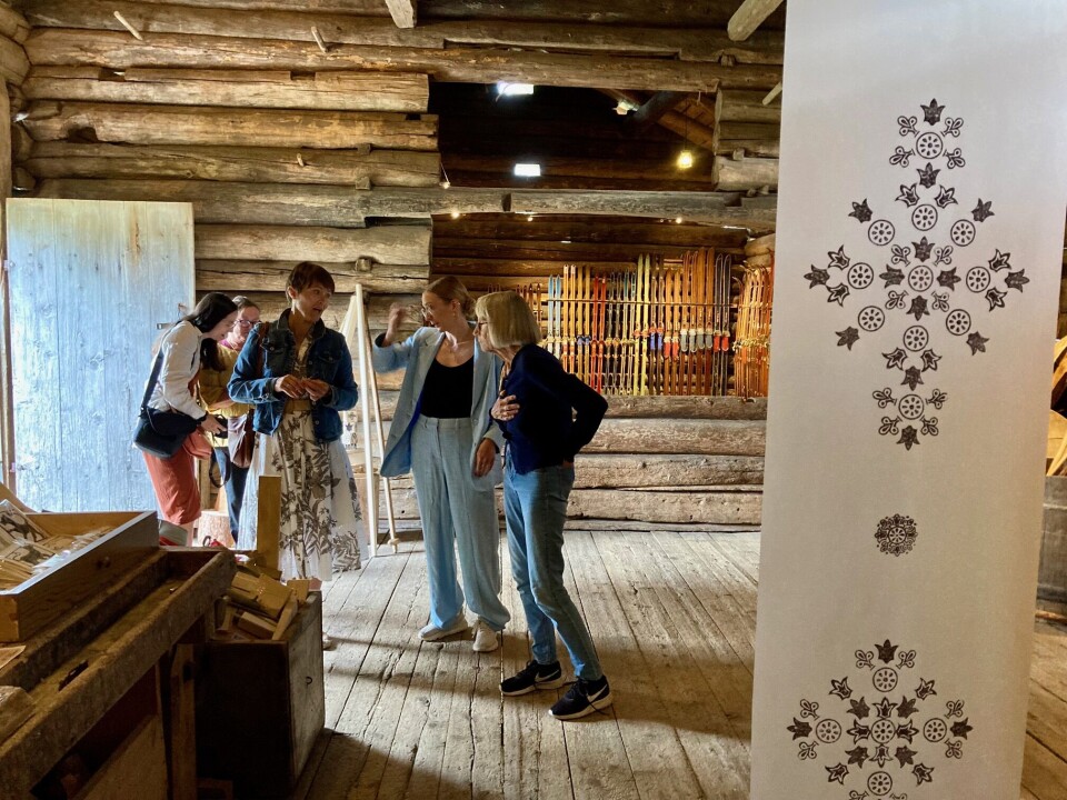 Sigrid Fivelstad forteller villig om sine prosjekter og idéer Sigrid snakker med et par damer midt i rommet. Vi ser noen trykk på stoff som henger fra en bjelke i forgrunnen.