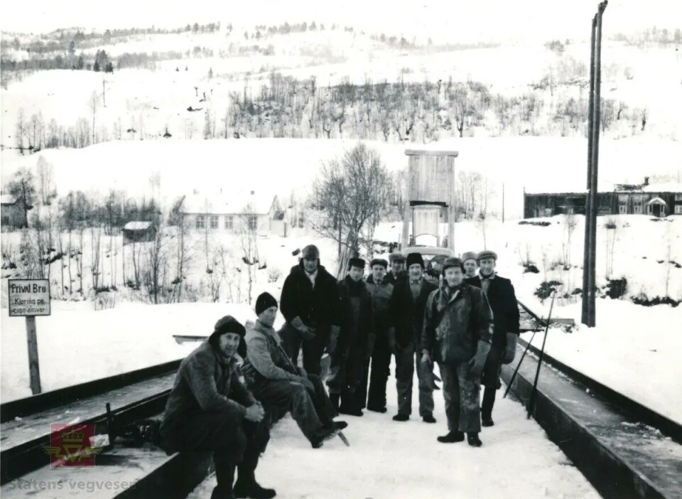 Det var andre arbeidsforhold den gangen gamle Dønheim bru ble bygget i 1953. Fra venstre: Olaf Gulla, Eirik Storholt, Lars H. Røv, Sivert Sande, Gunnar P. Sæter, Olaf Bredesen, Jo Fiske, Mikkel Aune (bas), Emil Fiske og Petter Dønnem. Svart-hvitt foto av arbeidsfolk på den nybygde veien på 50-tallet i et åpent og vinterkledd landskap.