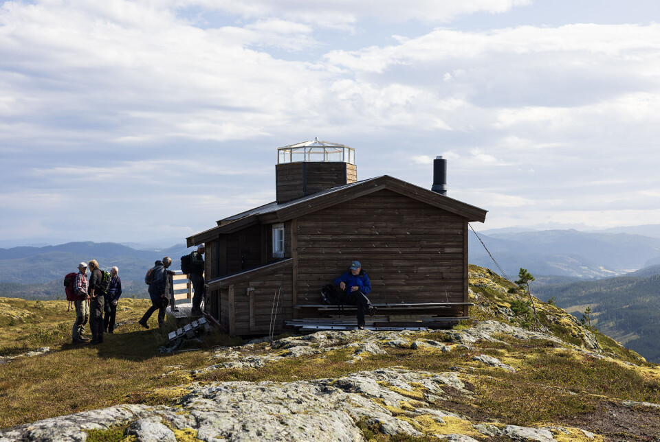 Vakthytta med tilbygg og tårn Flere personer ved ei hytte på en fjelltopp.