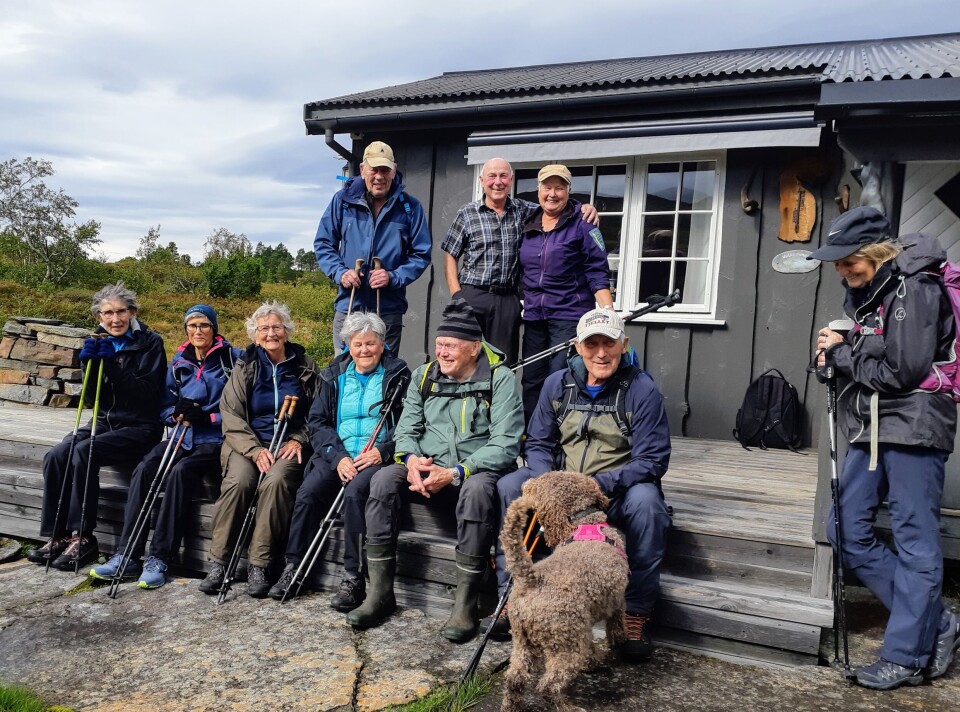 Stavgang til Sjøasetervatnet 10 turkledde personer og en hund foran ei hytte.