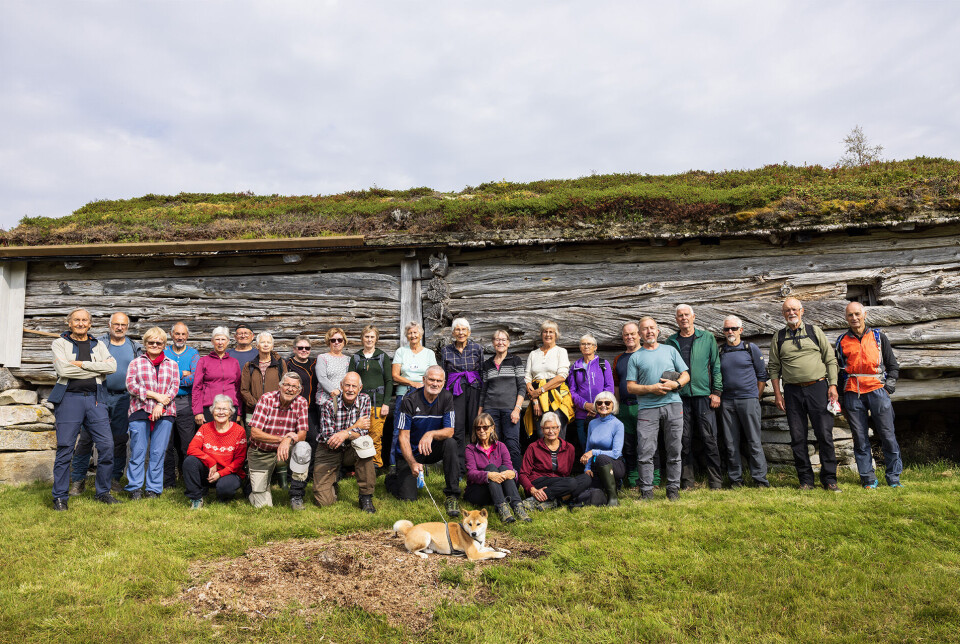 Furet og værbitt er og dei 28 framom seterfjøset. 28 turkledde folk oppstilt for fotografering foran et gammelt seterfjøs.