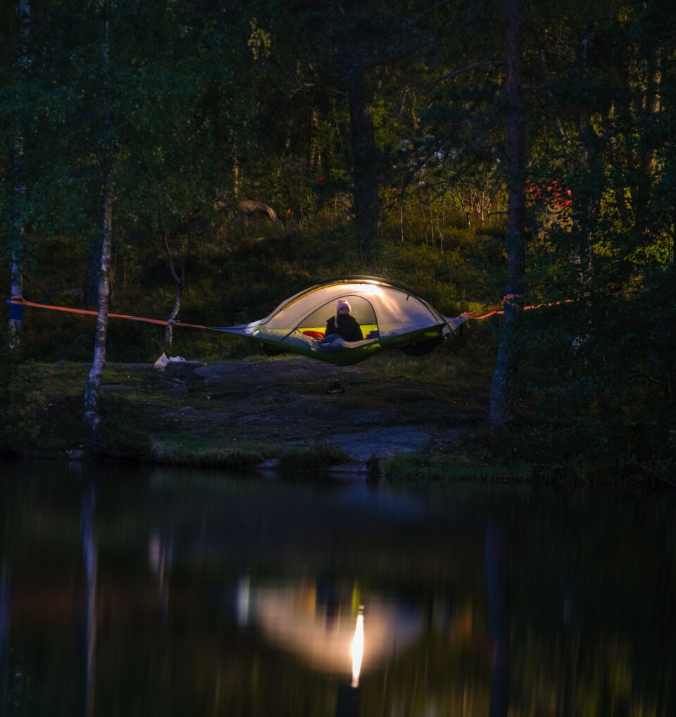 Natt i Naturen En overbygd hengekøye med lys og en person inni. Utenfor er det mørkt.