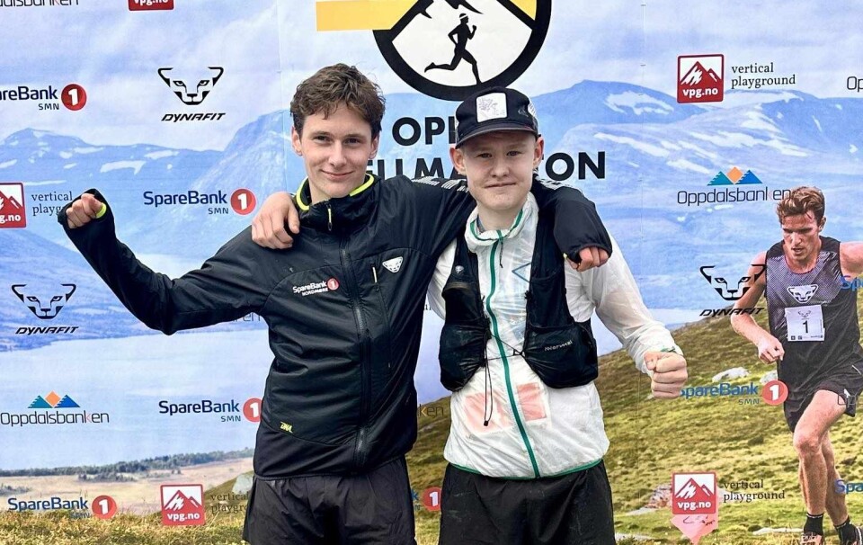 Aron Rodal Haugen og Isak Drøpping. To unge gutter med shorts og skitne joggesko etter fjellmaraton. De står foran et stort reklamefoto for løpet med sponsorer bak.