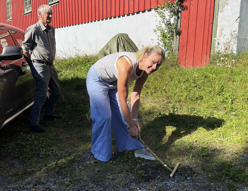 Gjertrud Heggem med «alna», klar til å vippe «jeppen» (kvemsen) som ligg oppå «hullu». Bak: Lars Sjøflot – som dreiv denne sporten for snart 80 år sia Dame står klar til å vippe pinne