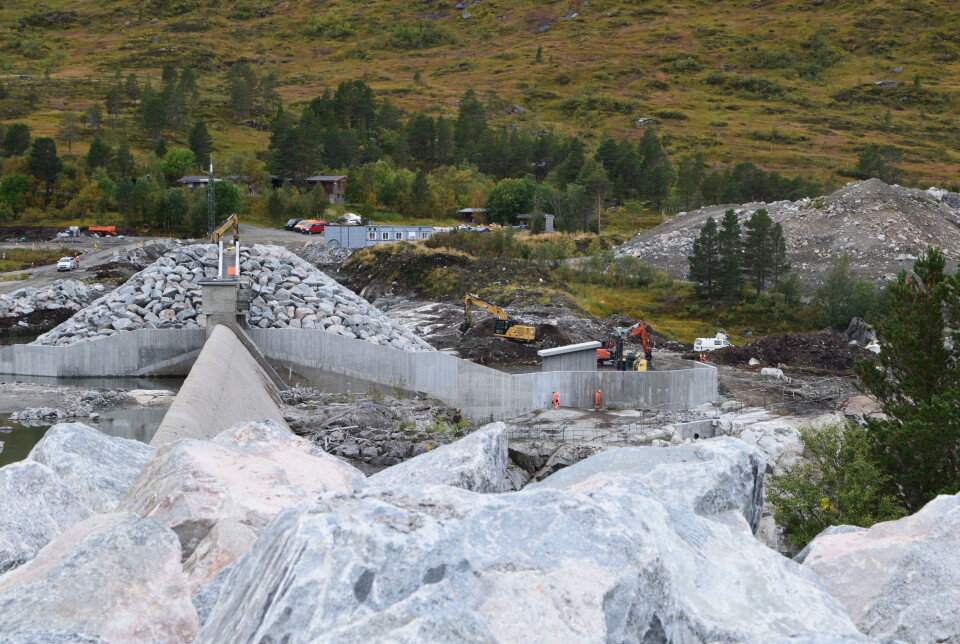 Gravemaskiner som legger masse inntil lekkasjemålehuset ved Gråhaugen. Bildet er tatt fra dammen. En del av en stor demning, og et par gravemaskiner som jobber ved siden av.