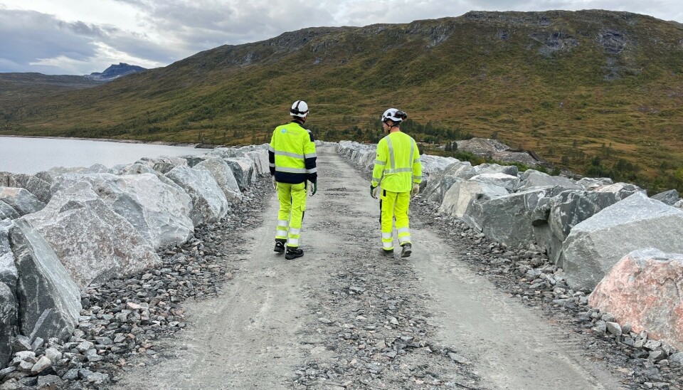Kjøring på Folldalsveien To menn i varselklær som går på en grusveg over en stor demning.