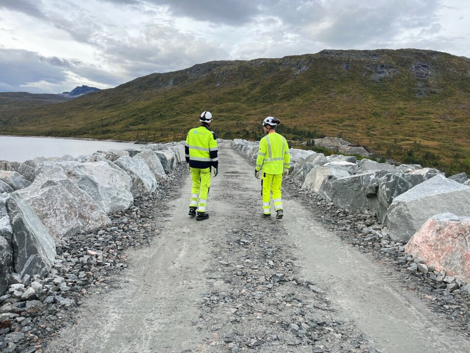 Arbeidet på Gråsjødammen er nesten ferdig. To menn i varselklær som går på en grusveg over en stor demning.