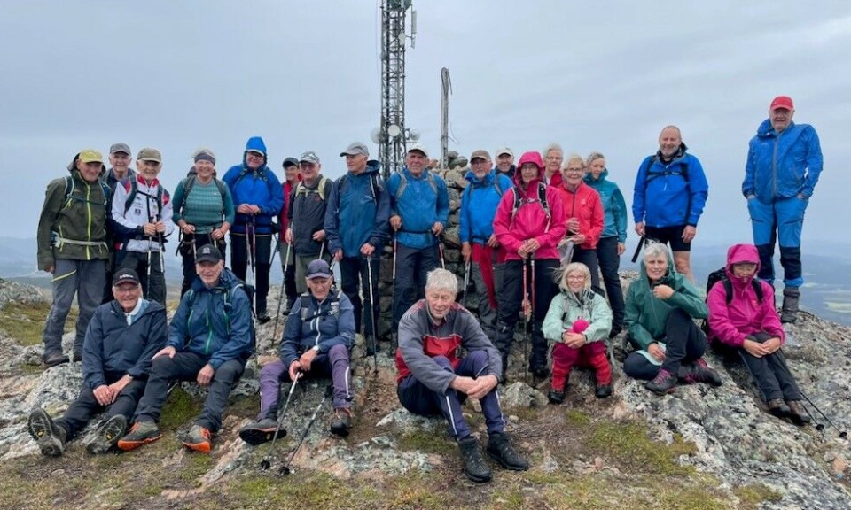 Tirsdagstur til Gimshøgda En gjeng med turkledde folk foran ei stor antenne på en fjelltopp, i grått vær.